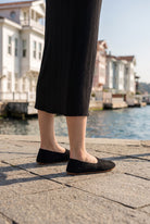 Woman in a black knit midi skirt wearing black barefoot ballet flats by Bespoky on a stone waterfront with white wooden mansions in Istanbul