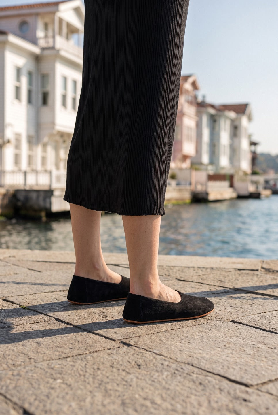 Woman in a black knit midi skirt wearing black barefoot ballet flats by Bespoky on a stone waterfront with white wooden mansions in Istanbul