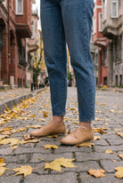 Person in light blue jeans wearing natural undyed leather barefoot sneakers by Bespoky on a cobblestone street with autumn leaves in Istanbul
