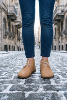 Person in dark jeans wearing natural undyed leather barefoot ankle boots by Bespoky on a snowy cobblestone street in Istanbul
