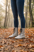 Person in dark skinny jeans wearing beige leather lace-up barefoot boots by Bespoky on a forest path covered in autumn leaves