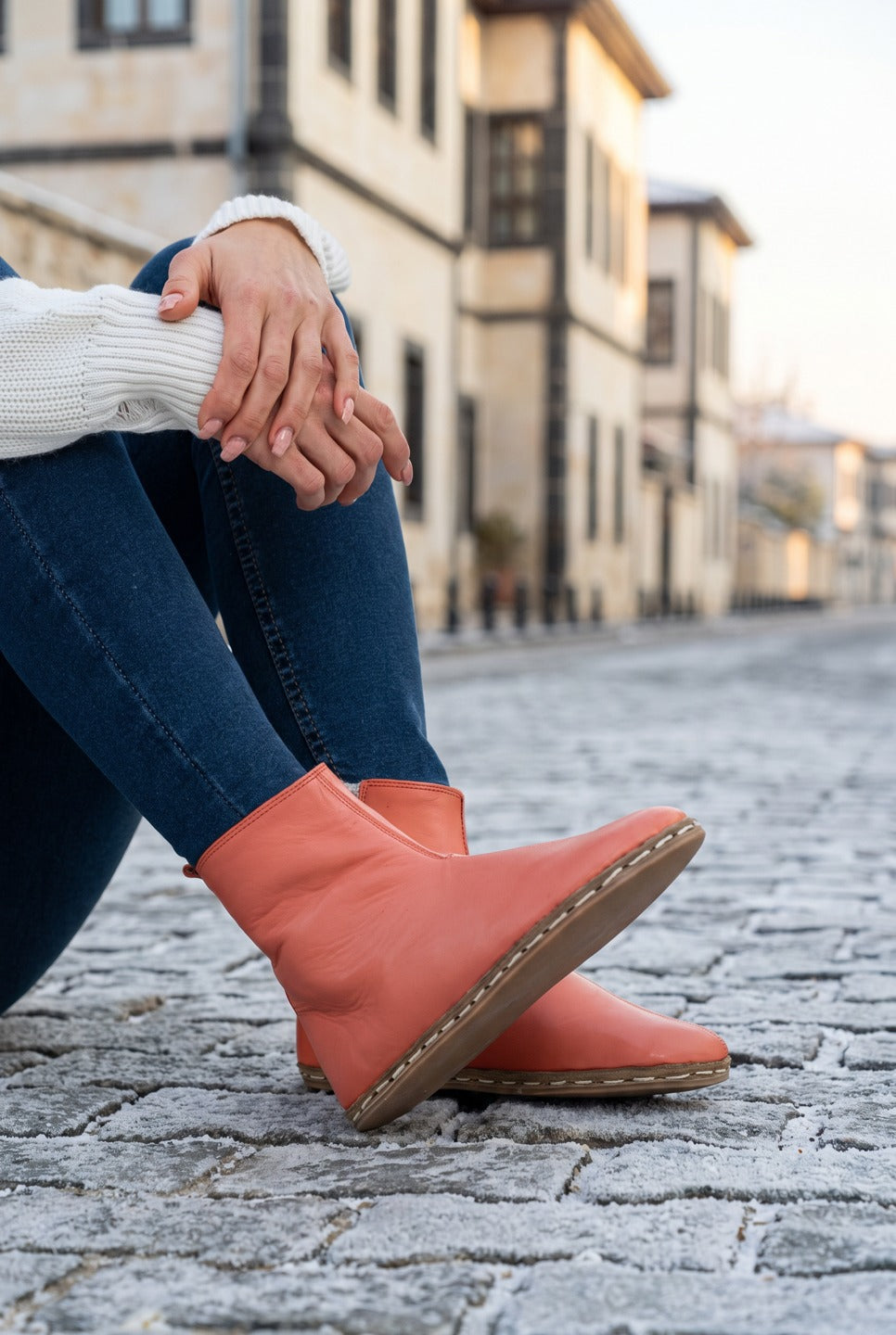 Woman in dark jeans and a cream sweater wearing pomegranate red leather barefoot boots by Bespoky on a frosty cobblestone street in Gaziantep