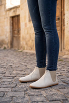 Woman in dark skinny jeans wearing cream leather barefoot chelsea boots by Bespoky on a cobblestone lane in a Cappadocia stone village