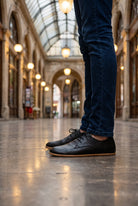 Man in dark jeans wearing black leather barefoot oxford shoes by Bespoky on the polished floor of a historic glass-roofed arcade in Istanbul