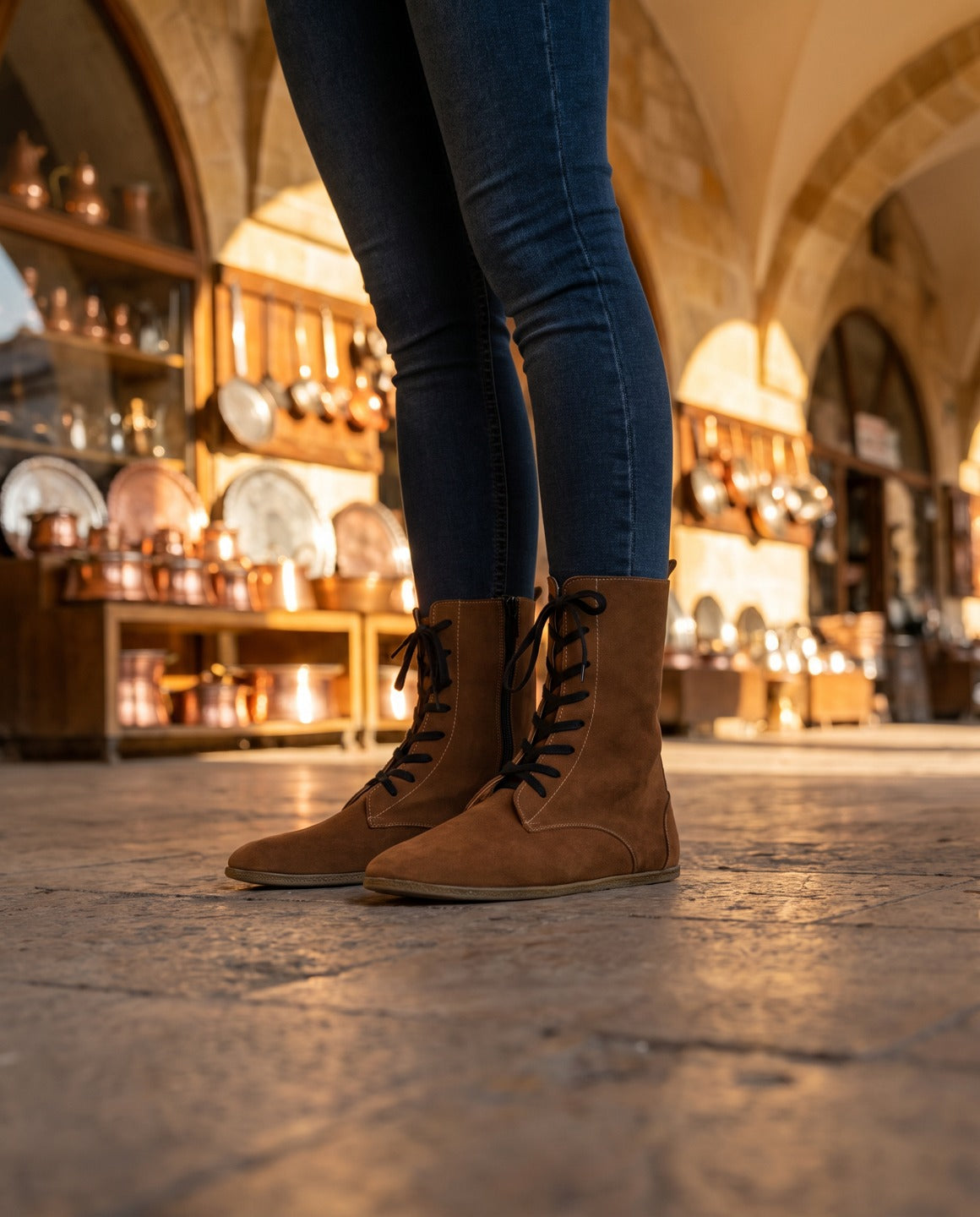 Women's tan lace-up barefoot ankle boots in the coppersmiths' bazaar of Gaziantep (AI-assisted background, real Bespoky product) [S3-antep-carsi-tanbot_v1.png]